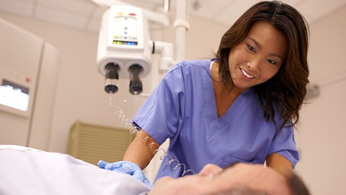 A medical professional in scrubs smiles at a patient lying on a table